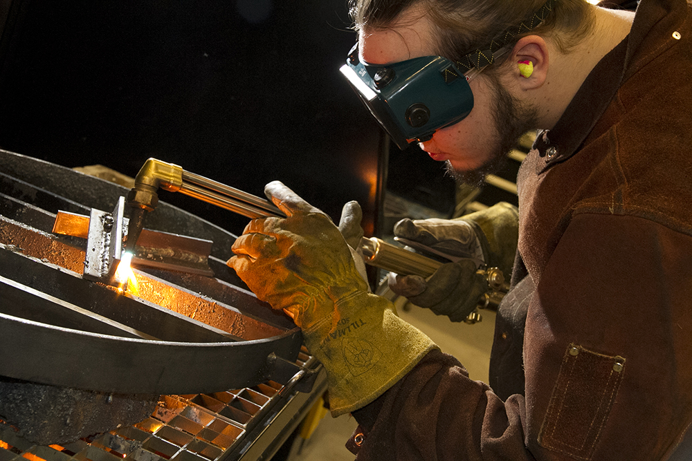 Man wearing safety goggles and gloves is intently welding metal.