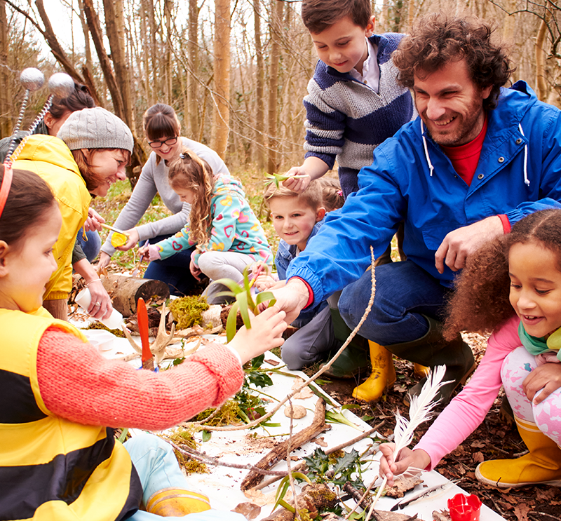 Volunteers in a forest setting leading young children in outdoor activities.