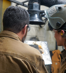 an over the shot photo of a student receiving feedback from a BWXT employee on their weld 