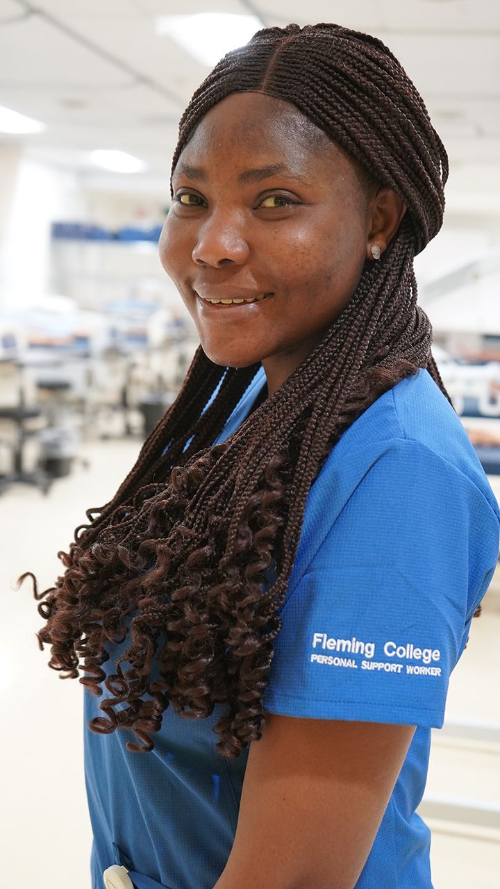 Image of a international student smiling and wearing a bright blue Personal Support Worker uniform.