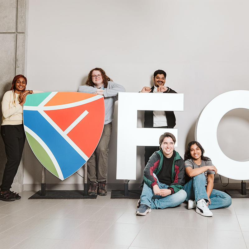 Five students sitting and standing around a large fleming logo sign.